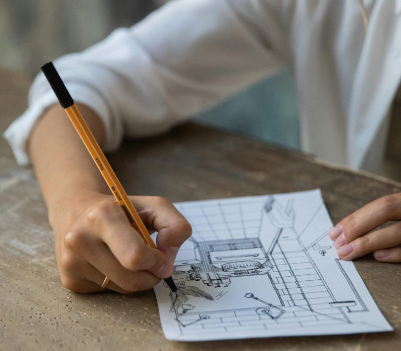 Close-up of a person sketching an interior design on a paper at a wooden table.